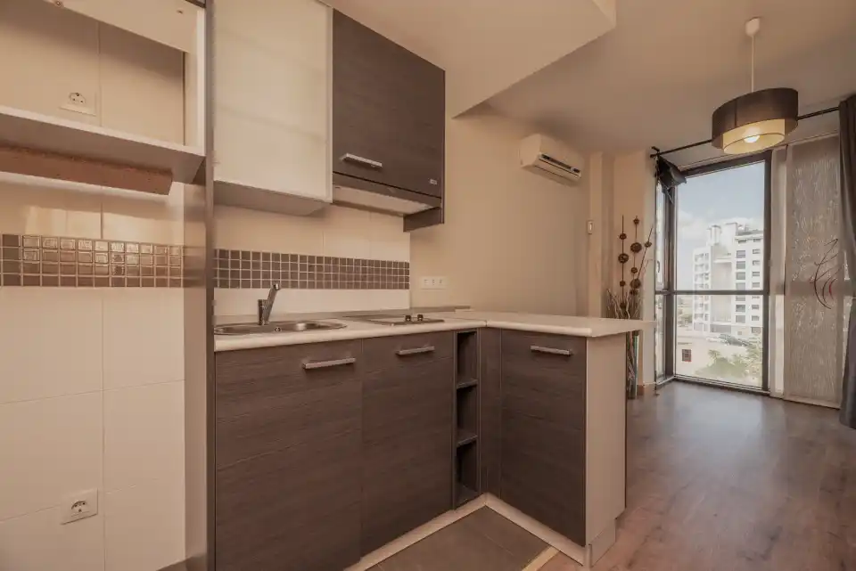 Cozinha planejada pequena com armários marrons, bancada amadeirada e revestimento claro, ideal para apartamentos em Campinas.